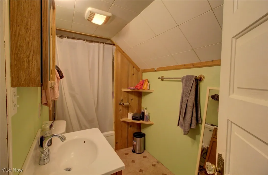 Full bath featuring a sink, vaulted ceiling, and curtained shower