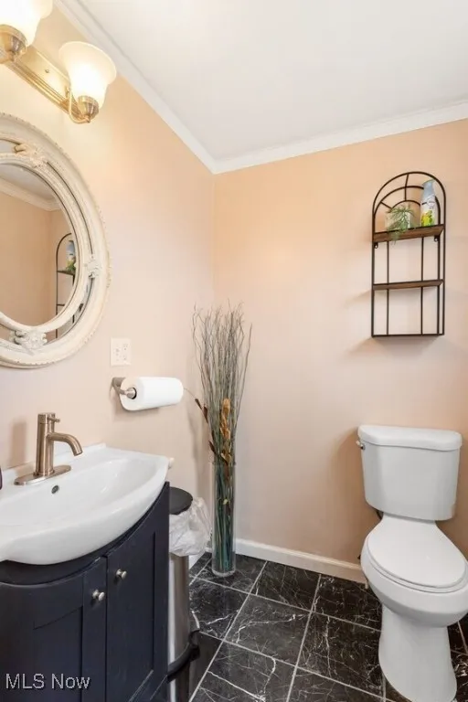 Bathroom with baseboards, vanity, ornamental molding, toilet, and marble look tiles