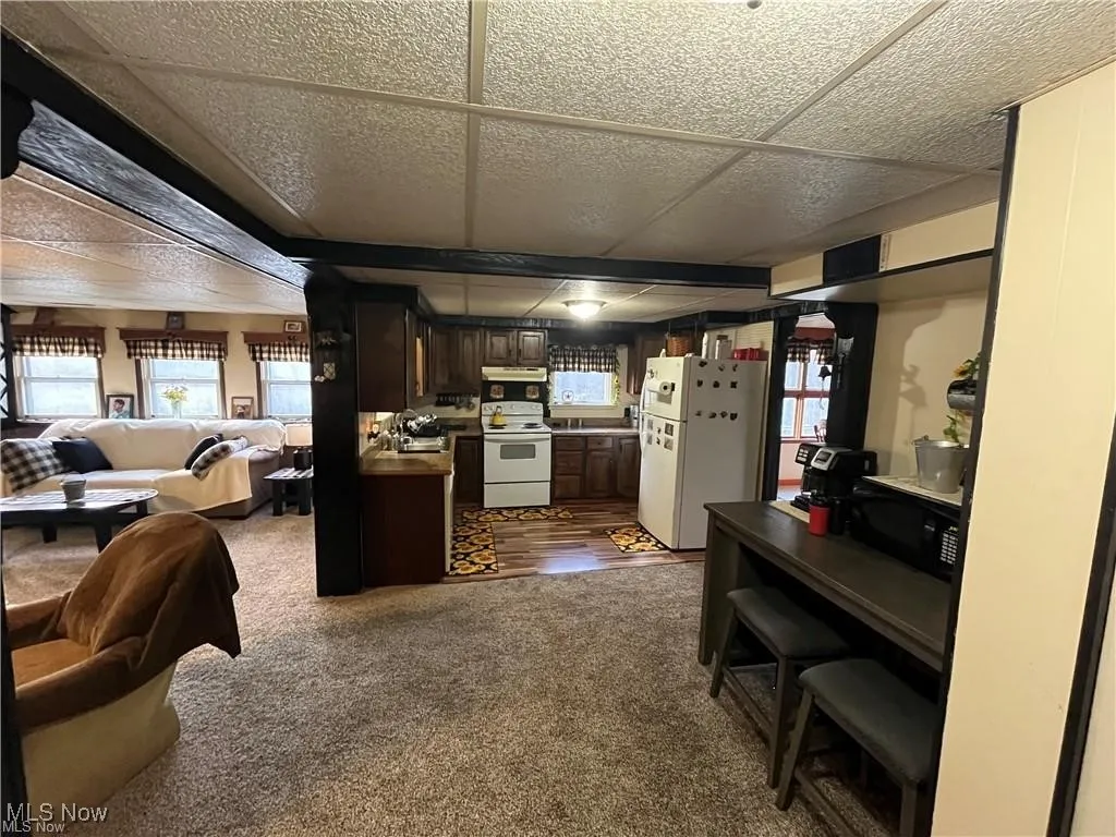 Kitchen featuring white appliances, open floor plan, plenty of natural light, dark brown cabinets, and a paneled ceiling