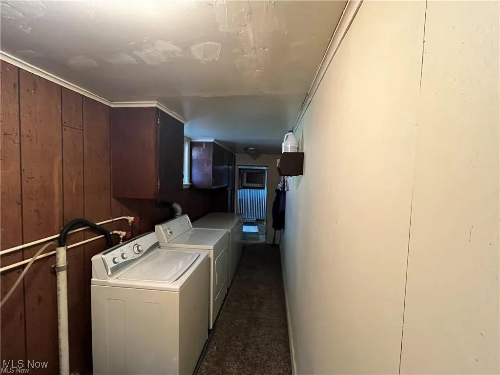 Laundry room featuring washing machine and dryer, cabinet space, wood walls, and carpet flooring