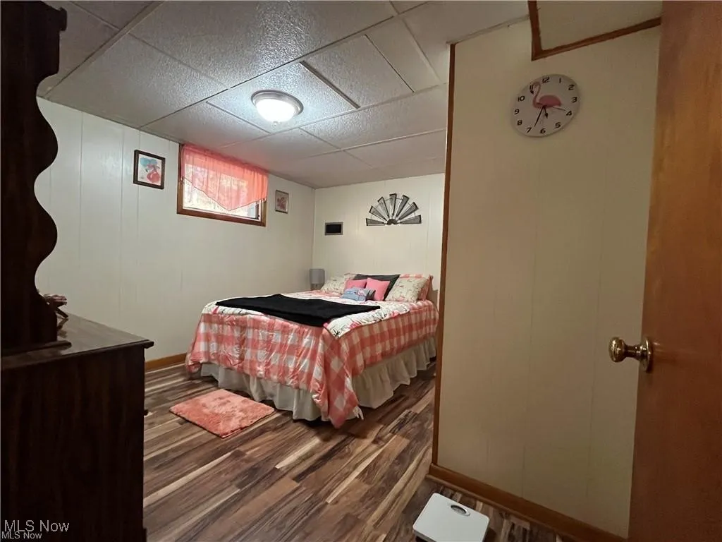 Bedroom with wood finished floors, a paneled ceiling, and baseboards
