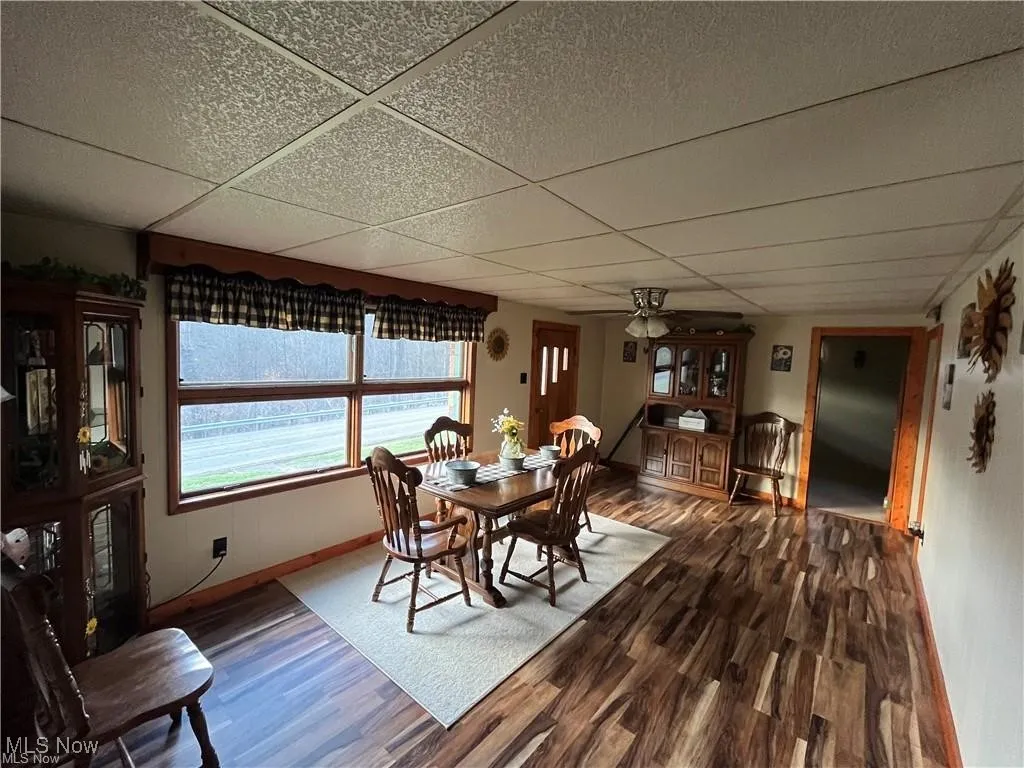 Dining space with dark wood-type flooring, a paneled ceiling, baseboards, and ceiling fan