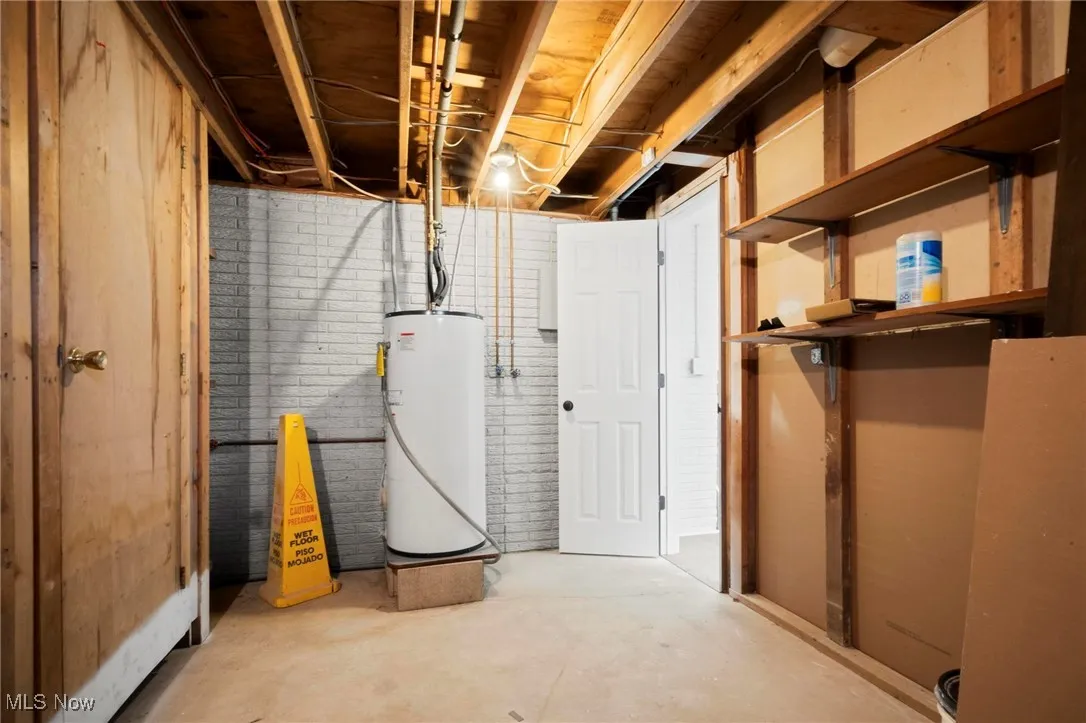 Unfinished below grade area with electric water heater and brick wall
