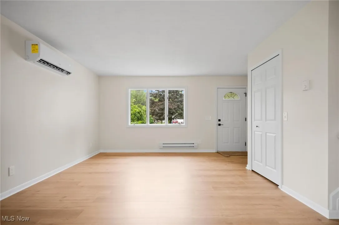 Empty room with an AC wall unit, light wood-type flooring, a baseboard radiator, and baseboards