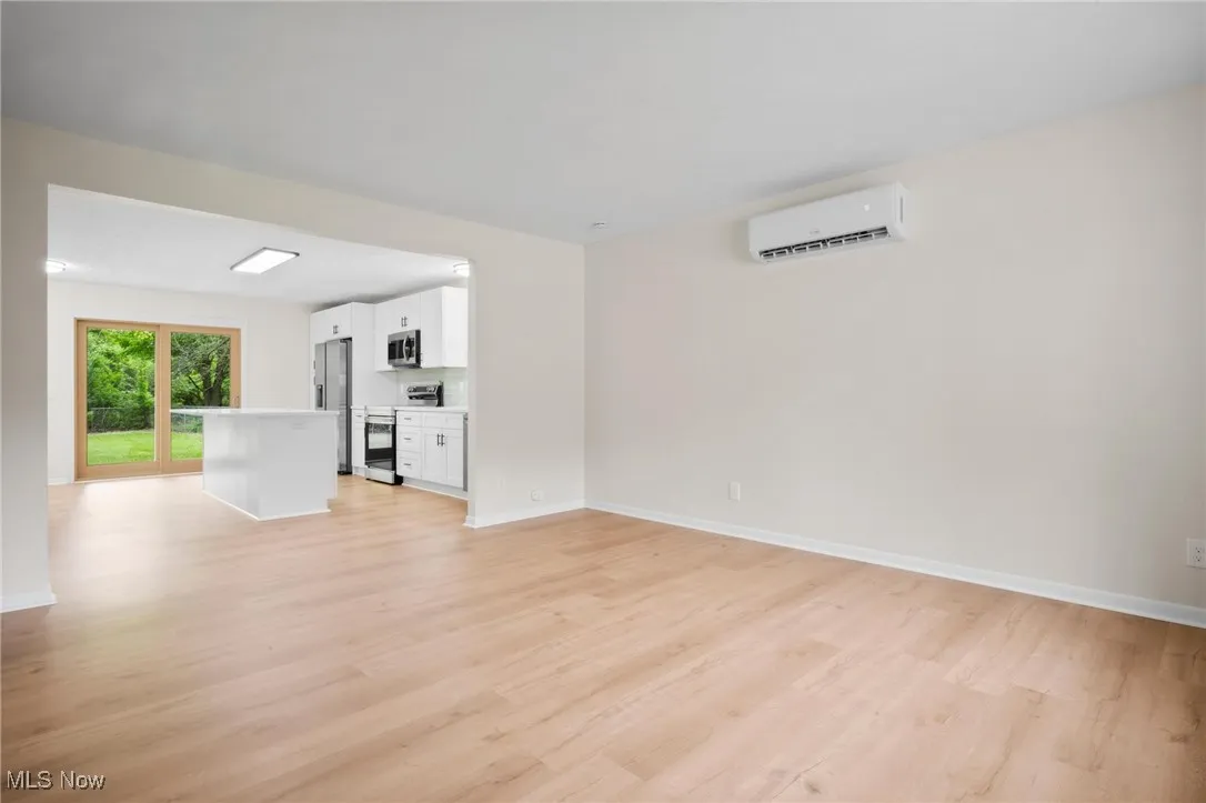 Unfurnished living room with a wall unit AC, light wood finished floors, and baseboards