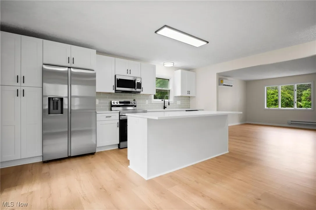 Kitchen with appliances with stainless steel finishes, light wood-type flooring, a baseboard radiator, and tasteful backsplash