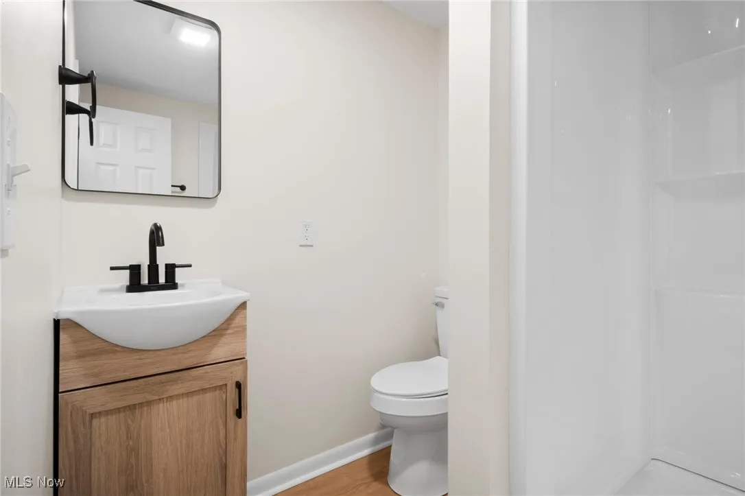 Full bath with toilet, vanity, a shower, baseboards, and wood finished floors