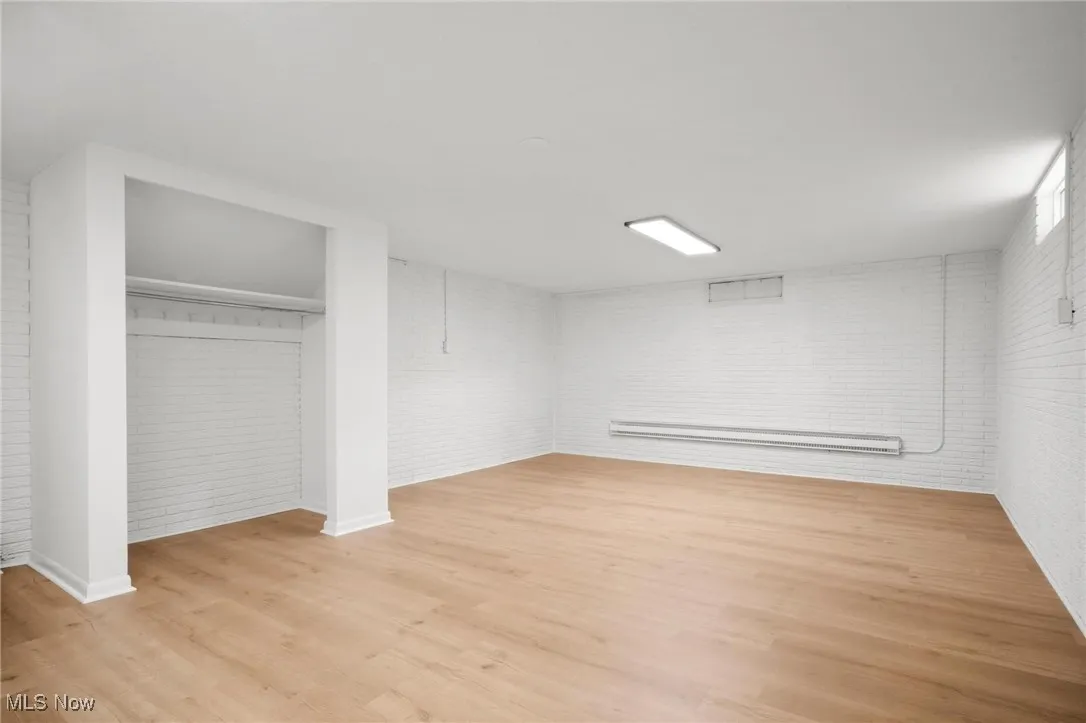 Finished below grade area featuring a baseboard radiator, wood finished floors, and brick wall