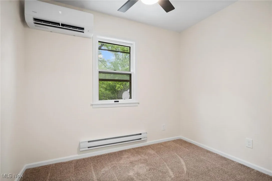 Empty room featuring baseboard heating, an AC wall unit, carpet floors, and baseboards