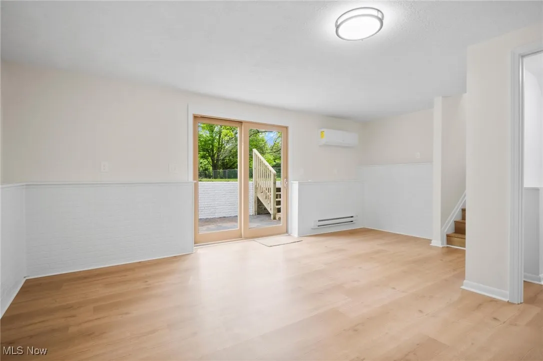 Unfurnished room featuring an AC wall unit, a baseboard radiator, wood finished floors, wainscoting, and stairs