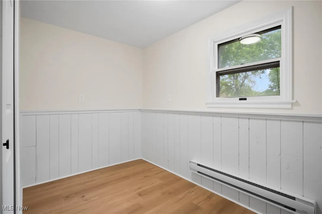 Spare room featuring baseboard heating, a wainscoted wall, and light wood finished floors