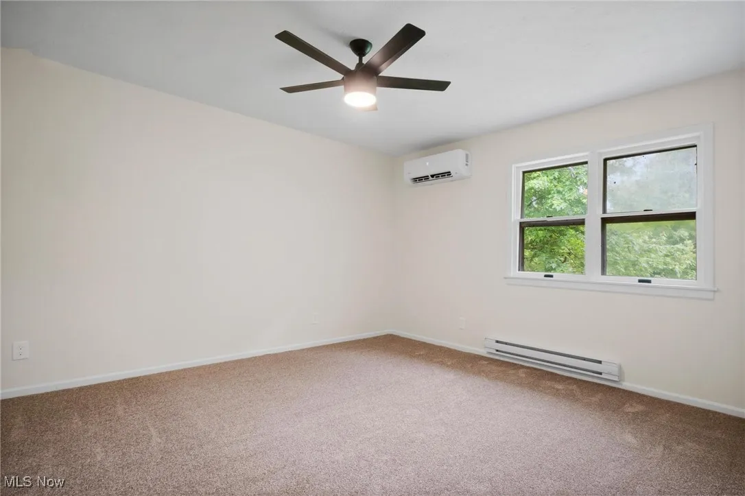 Spare room with a baseboard heating unit, an AC wall unit, carpet flooring, a ceiling fan, and baseboards