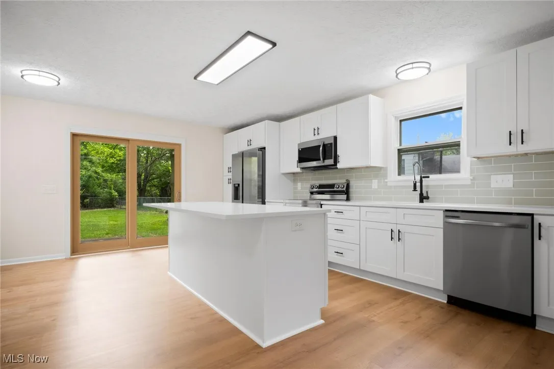 Kitchen with stainless steel appliances, backsplash, light wood-style floors, a center island, and light countertops