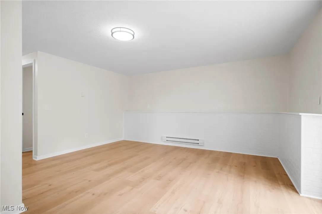 Unfurnished room featuring a baseboard heating unit, light wood-style flooring, and baseboards