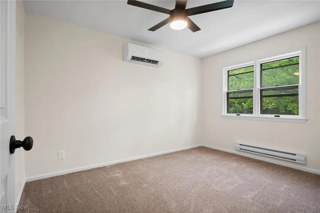 Unfurnished room with a baseboard heating unit, a wall mounted AC, carpet flooring, and ceiling fan