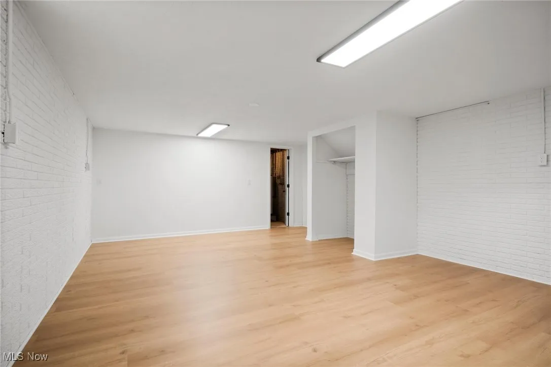 Finished below grade area featuring light wood-style floors, brick wall, and baseboards