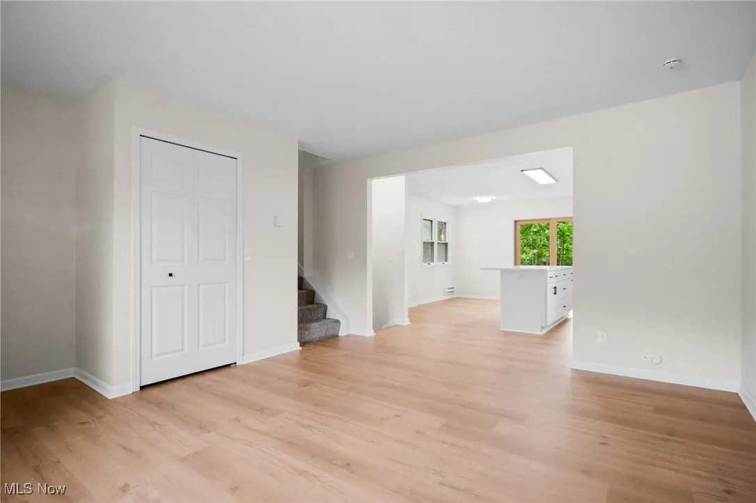 Unfurnished living room with light wood-type flooring, stairway, and baseboards