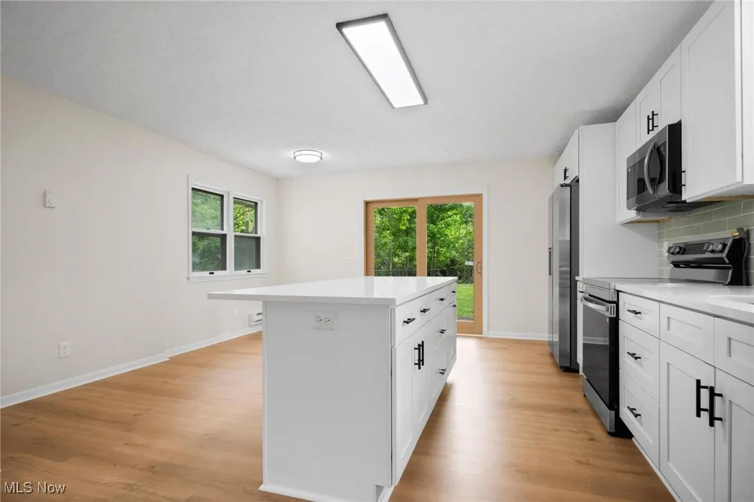 Kitchen with stainless steel appliances, a center island, light countertops, backsplash, and baseboards