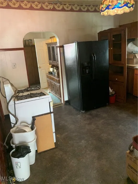 Kitchen featuring freestanding refrigerator, finished concrete floors, range, and wainscoting
