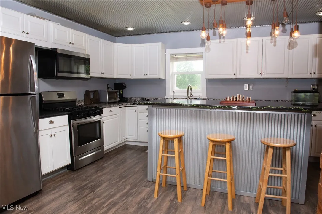 Kitchen with stainless steel appliances, dark wood-style flooring, white cabinetry, a kitchen breakfast bar, and a center island