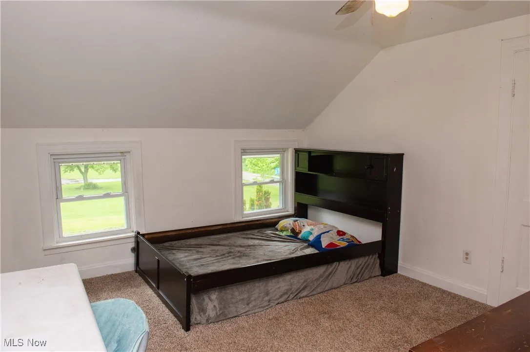 Bedroom with vaulted ceiling, carpet flooring, multiple windows, and baseboards