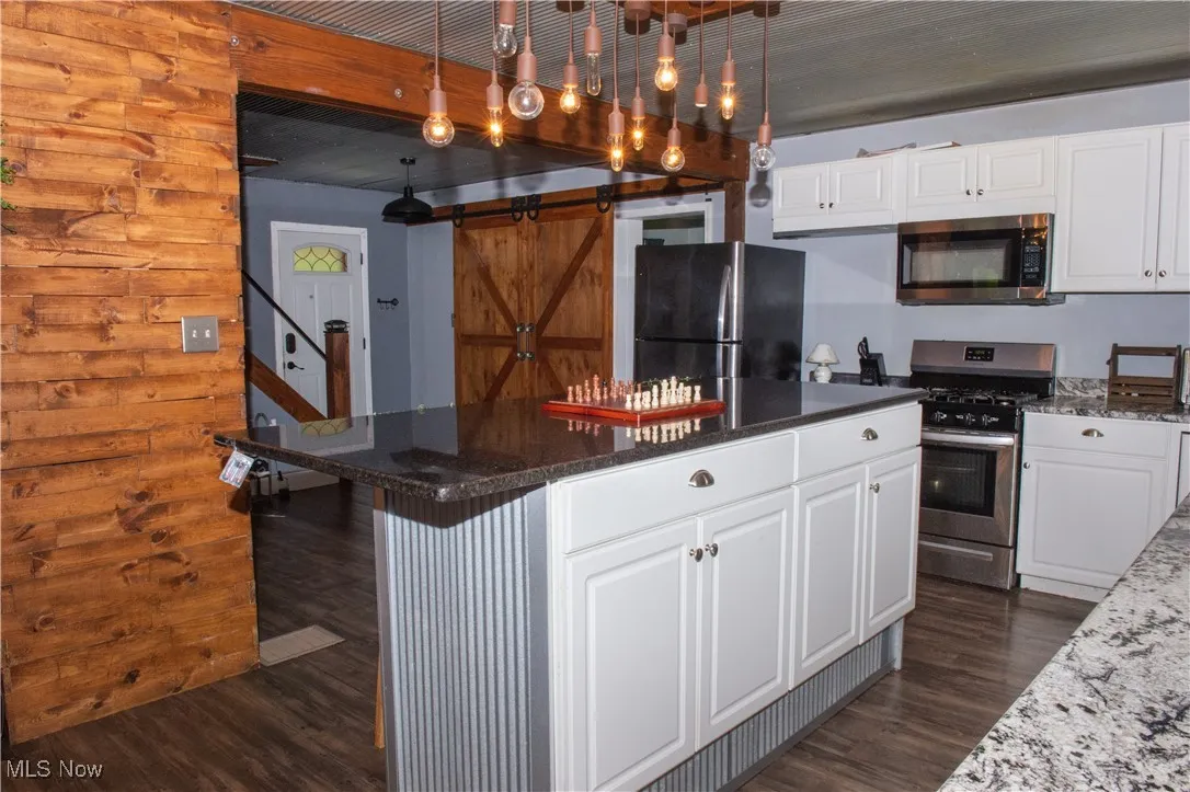 Kitchen with appliances with stainless steel finishes, dark wood-style flooring, a center island, and white cabinetry