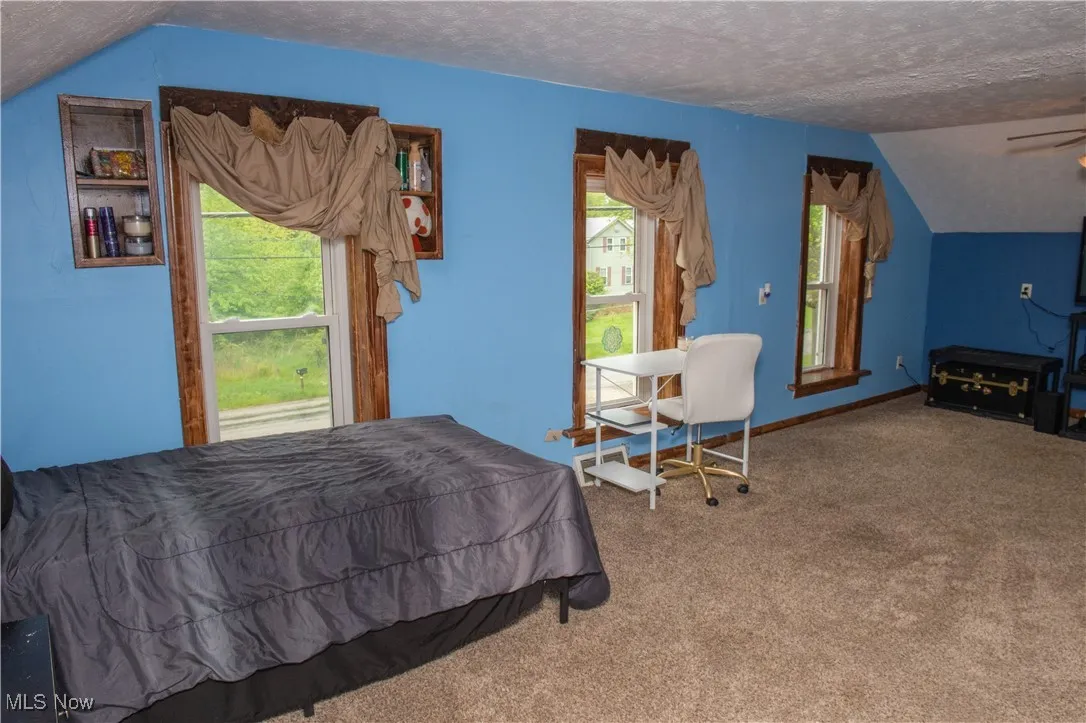 Carpeted bedroom featuring a textured ceiling, vaulted ceiling, and multiple windows