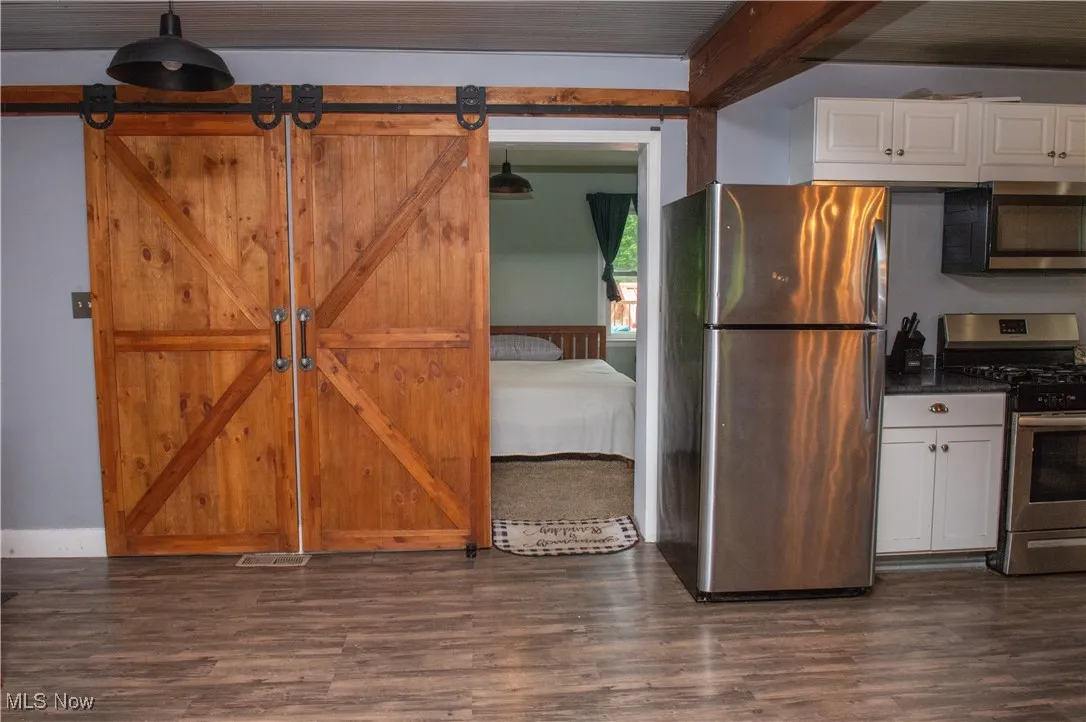 Kitchen with stainless steel appliances, white cabinetry, dark wood-type flooring, dark countertops, and a barn door