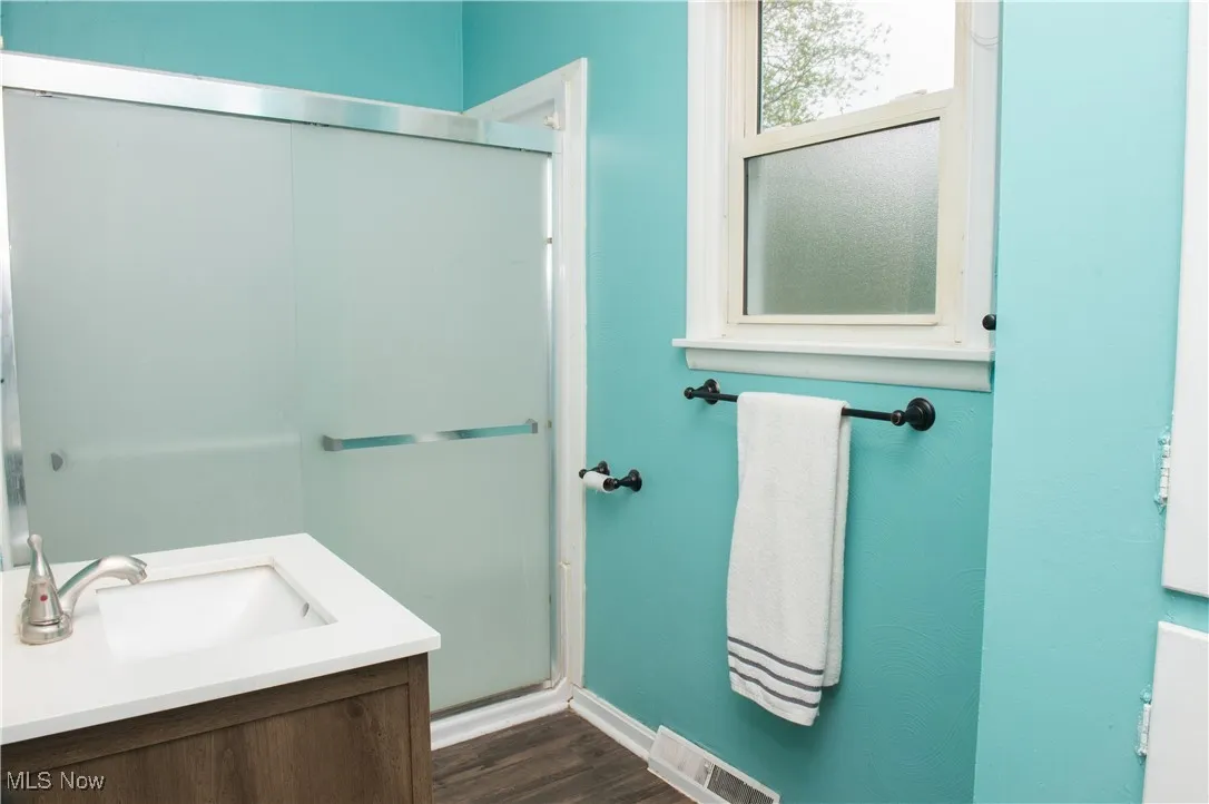 Bathroom featuring wood finished floors, a shower stall, baseboards, and vanity