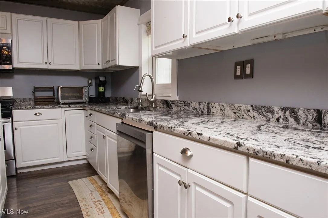 Kitchen with stainless steel appliances, white cabinets, a sink, dark wood-style floors, and light stone countertops