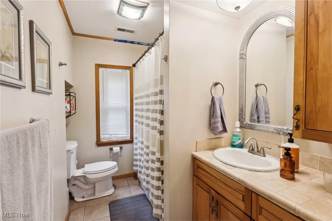 Full bathroom with toilet, vanity, tile patterned floors, and a shower with curtain