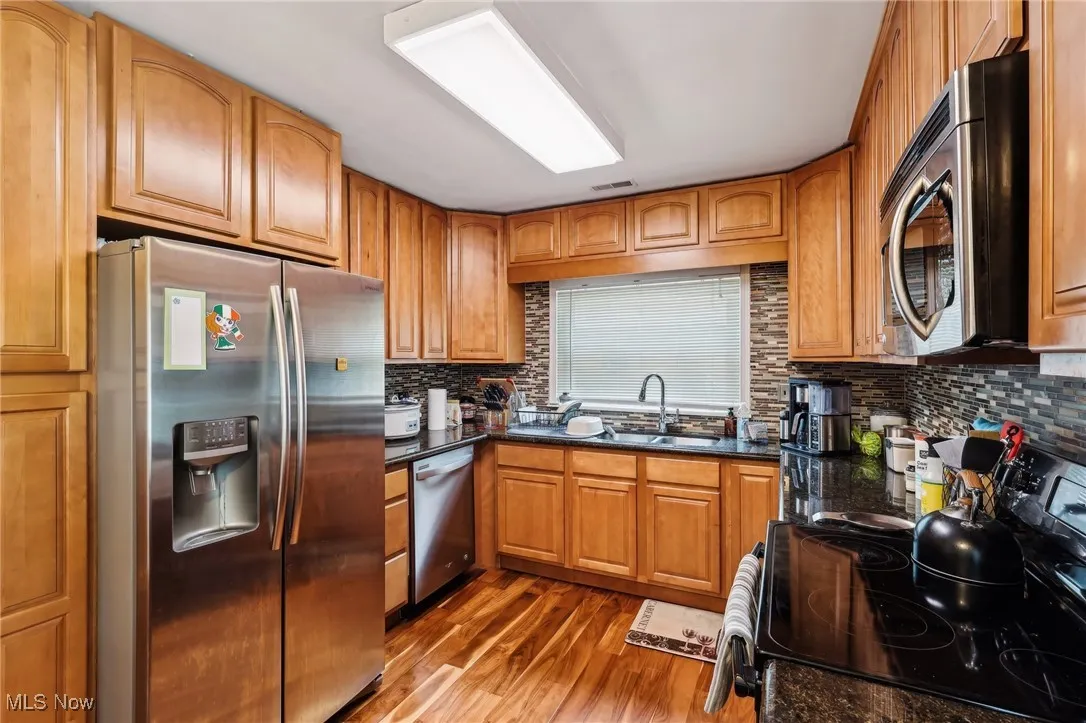 Kitchen with appliances with stainless steel finishes, a sink, dark wood-type flooring, tasteful backsplash, and brown cabinetry