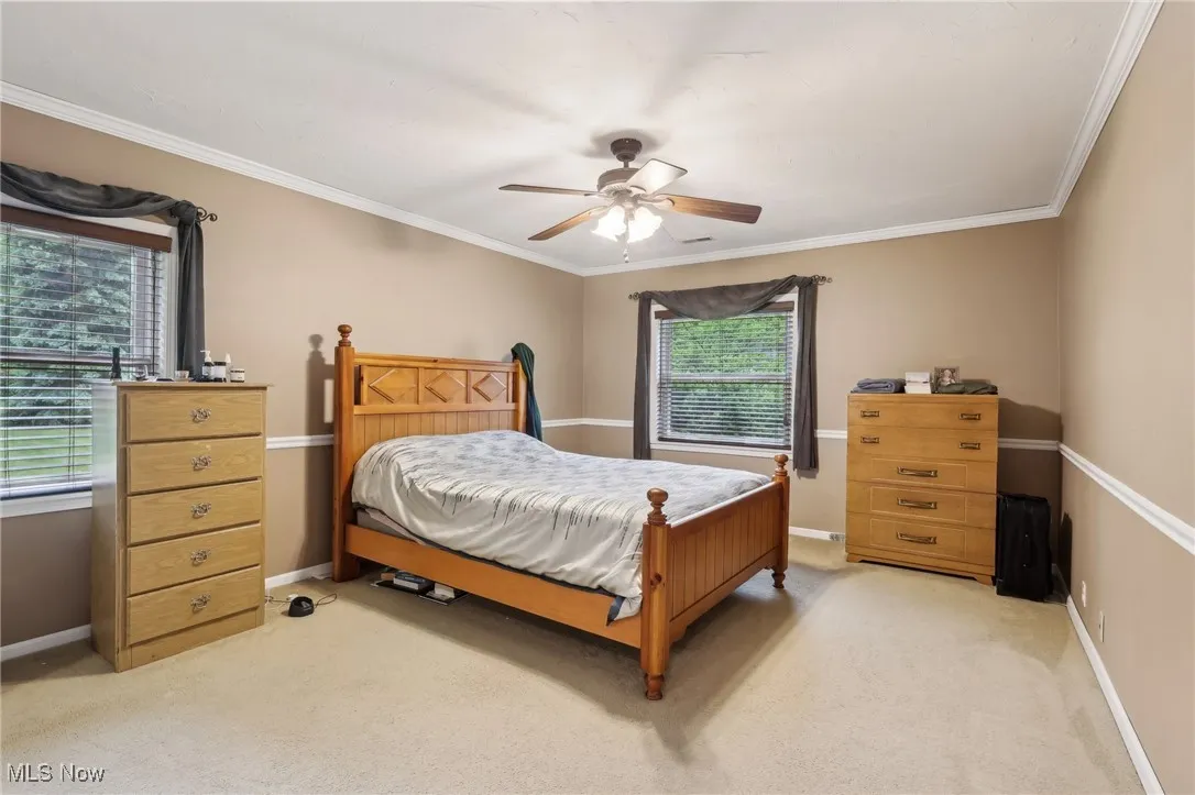 Bedroom with light colored carpet, baseboards, ornamental molding, and a ceiling fan