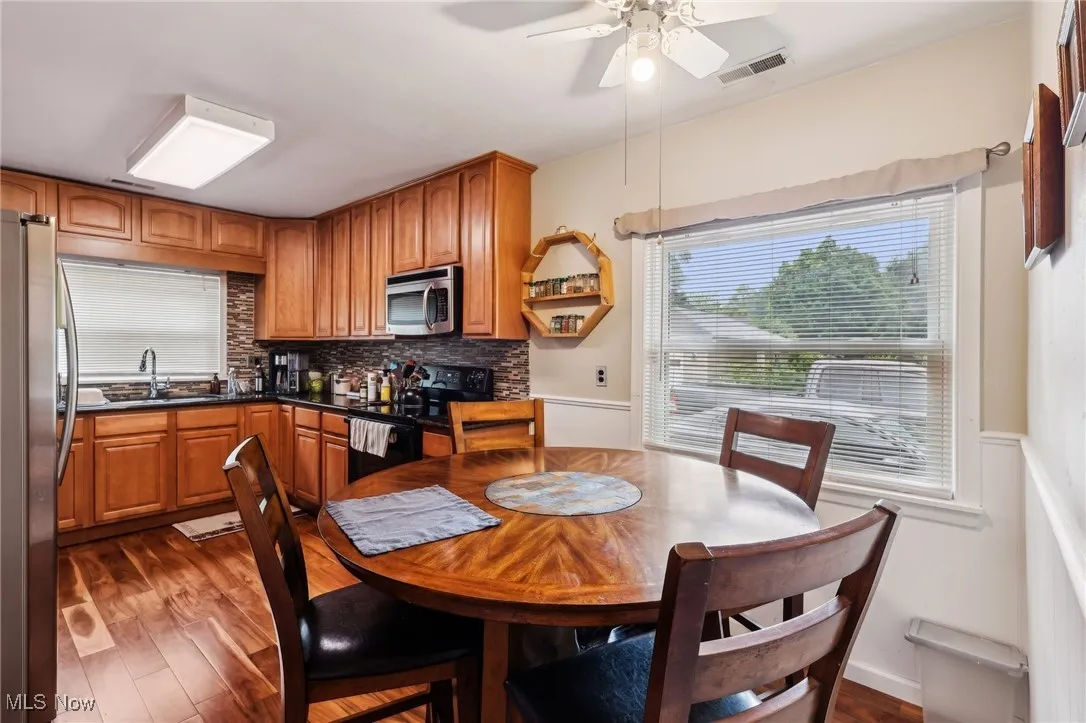 Dining room with ceiling fan, dark wood-style floors, and a wainscoted wall