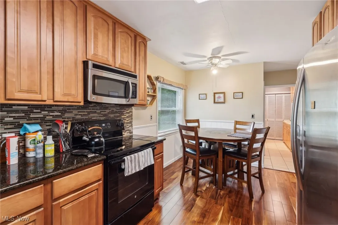Kitchen with stainless steel appliances, ceiling fan, decorative backsplash, wood finished floors, and dark stone counters