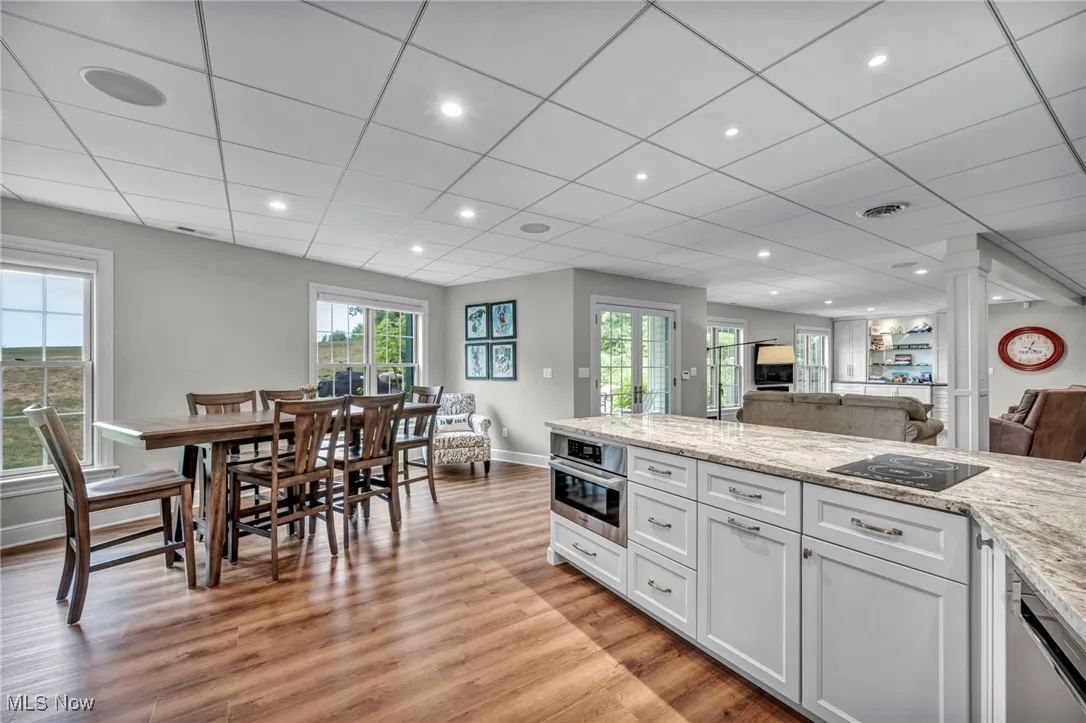 Kitchen with white cabinets, light stone countertops, light wood finished floors, healthy amount of natural light, and a drop ceiling