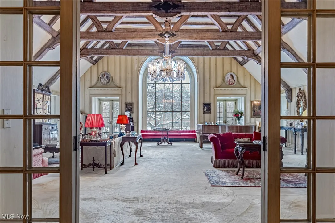 Sitting room with carpet, a chandelier, lofted ceiling with beams, french doors, and wood walls