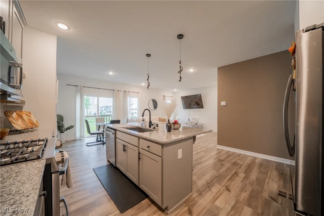 Kitchen featuring stainless steel appliances, a sink, light wood finished floors, recessed lighting, and a kitchen island with sink