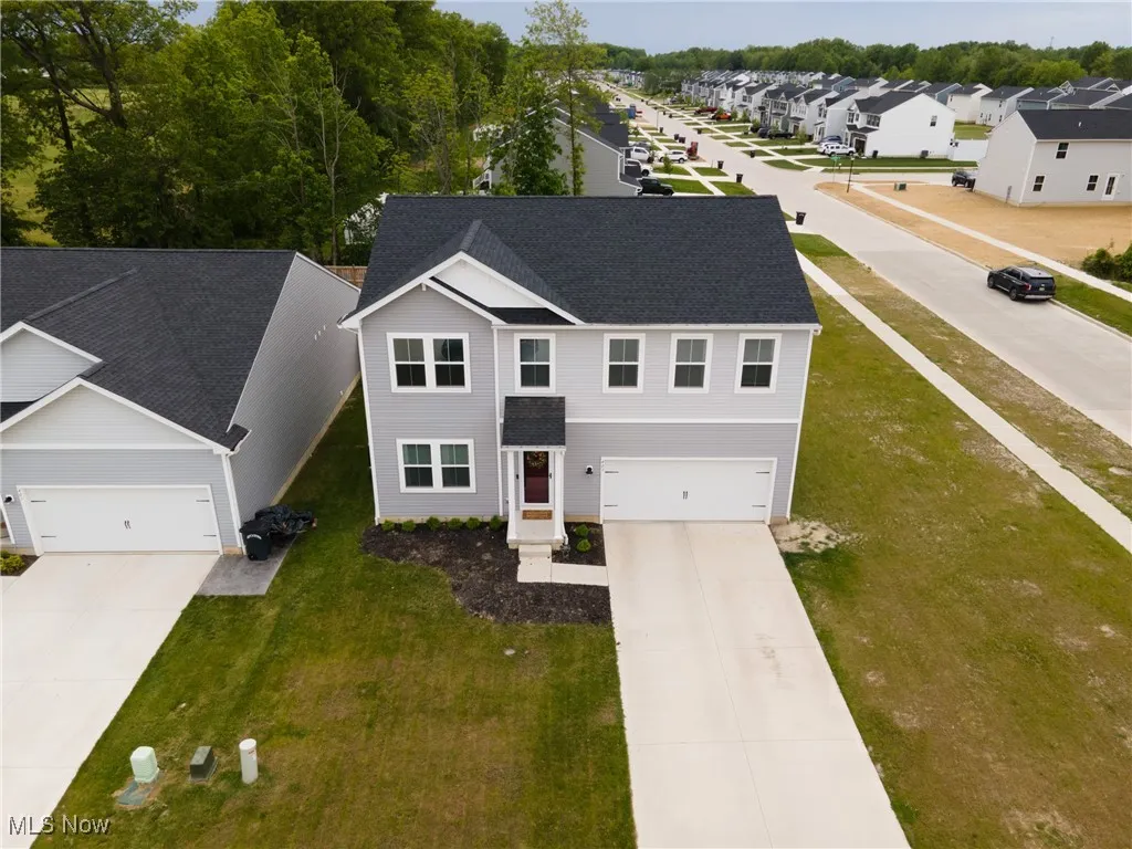 View of front facade with driveway, a front lawn, and roof with shingles