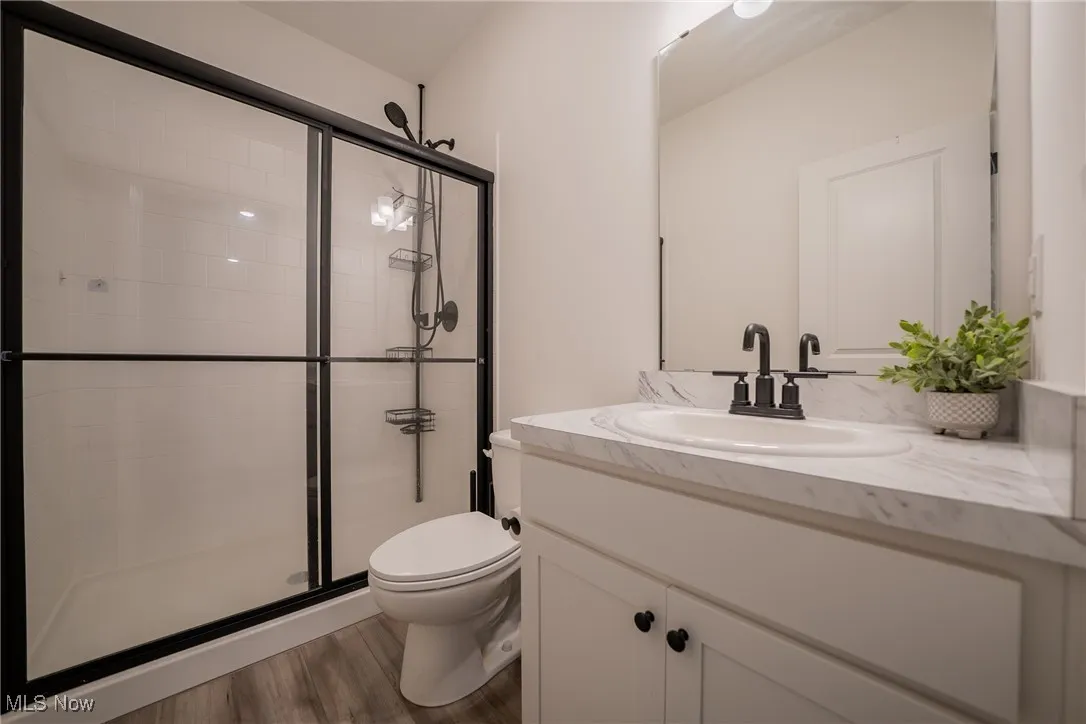 Full bath featuring toilet, vanity, a shower stall, and wood finished floors