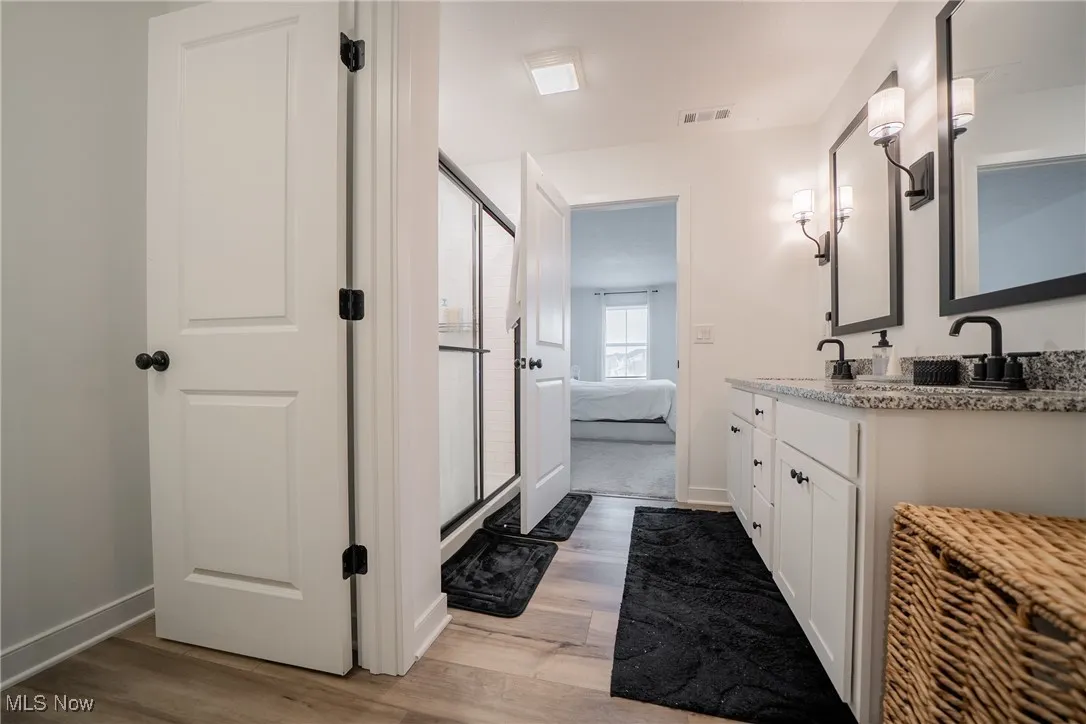 Ensuite bathroom featuring wood finished floors, double vanity, a shower stall, and baseboards