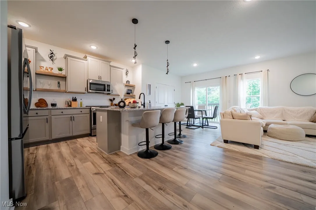 Kitchen featuring stainless steel appliances, open shelves, open floor plan, a kitchen breakfast bar, and light wood finished floors
