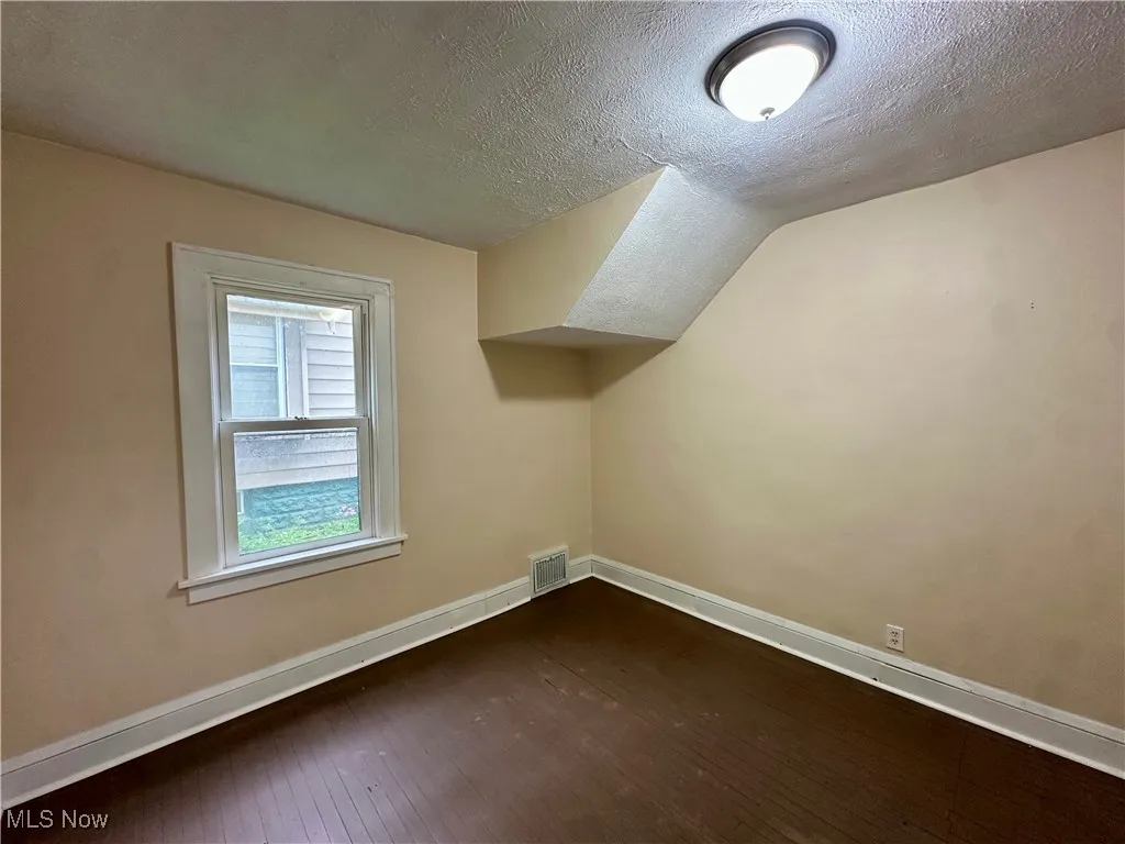 Additional living space featuring dark wood finished floors, baseboards, a textured ceiling, and vaulted ceiling