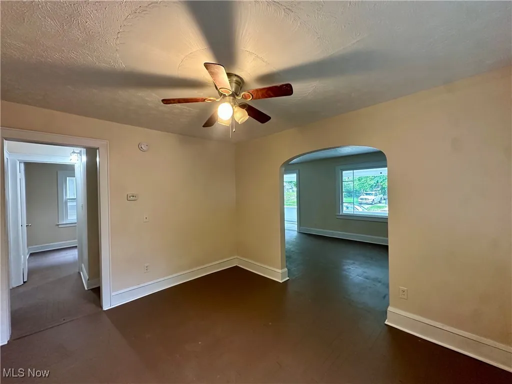 Spare room with arched walkways, a ceiling fan, and baseboards