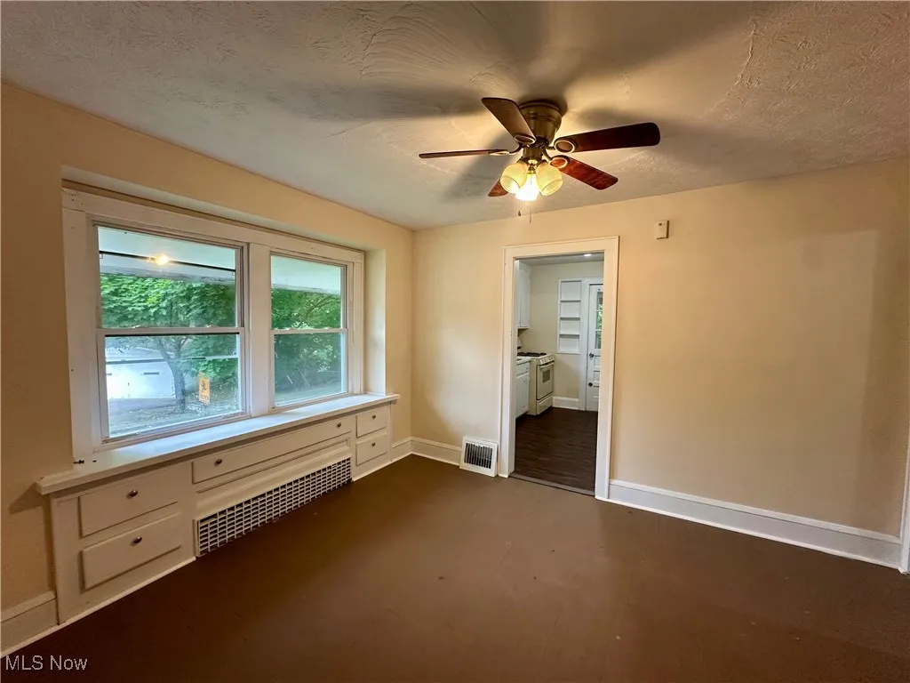 Empty room featuring baseboards, radiator, ceiling fan, a textured ceiling, and dark wood finished floors