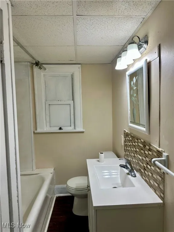 Bathroom featuring wood finished floors, toilet, a drop ceiling, vanity, and baseboards