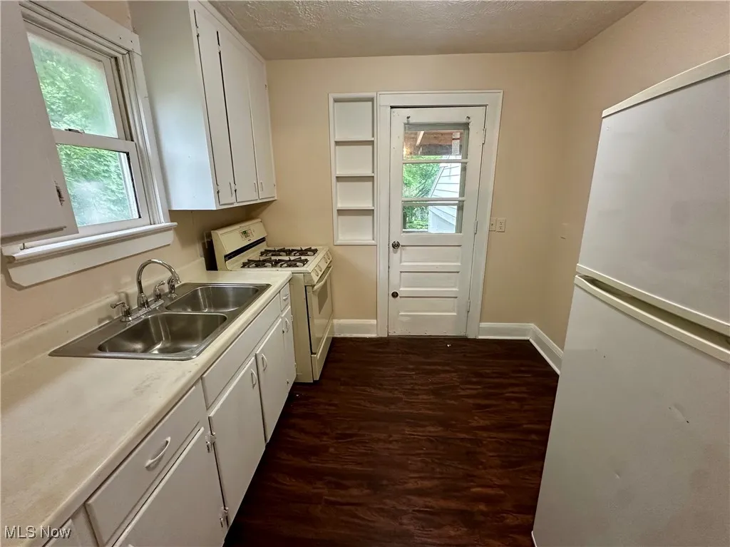 Kitchen with white appliances, a sink, dark wood-style floors, white cabinetry, and light countertops