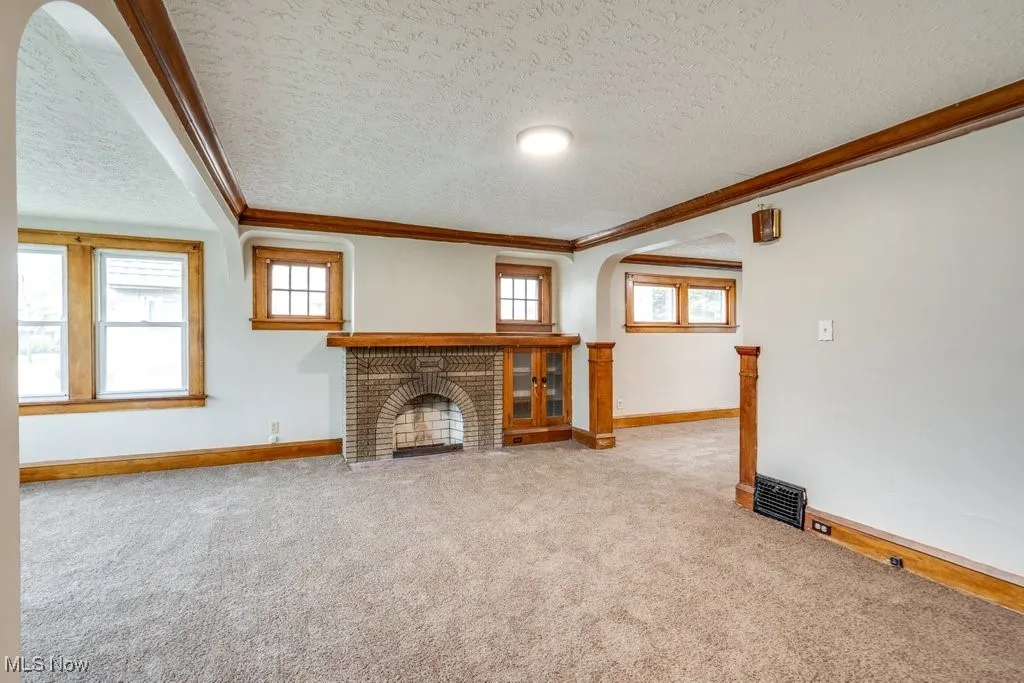 Unfurnished living room featuring ornamental molding, baseboards, carpet, a textured ceiling, and a brick fireplace