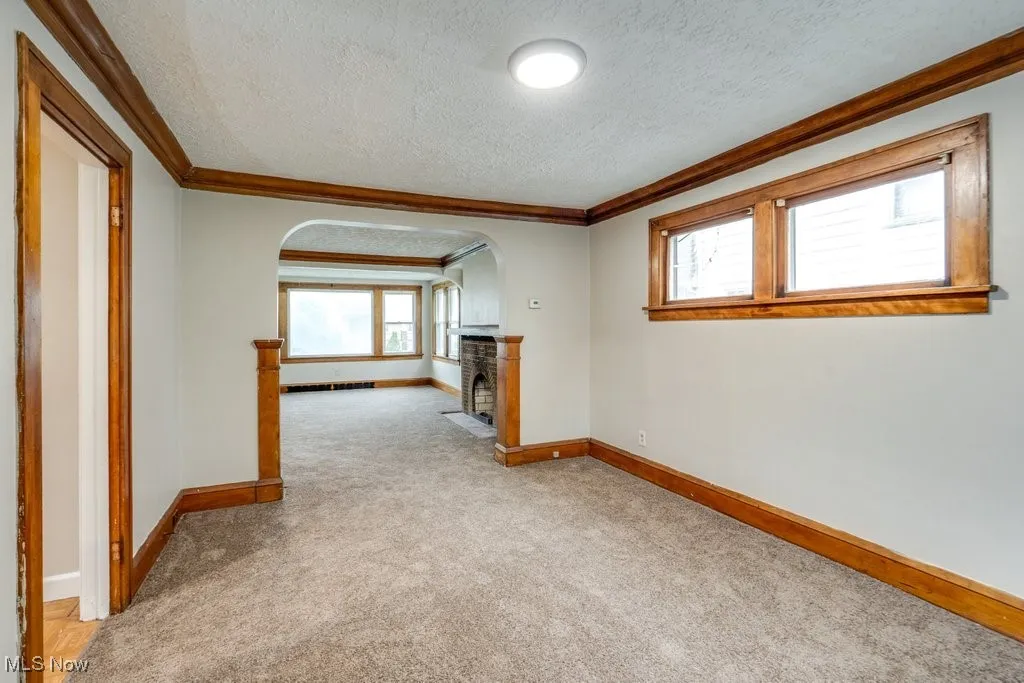 Unfurnished room with a textured ceiling, arched walkways, crown molding, baseboards, and light colored carpet