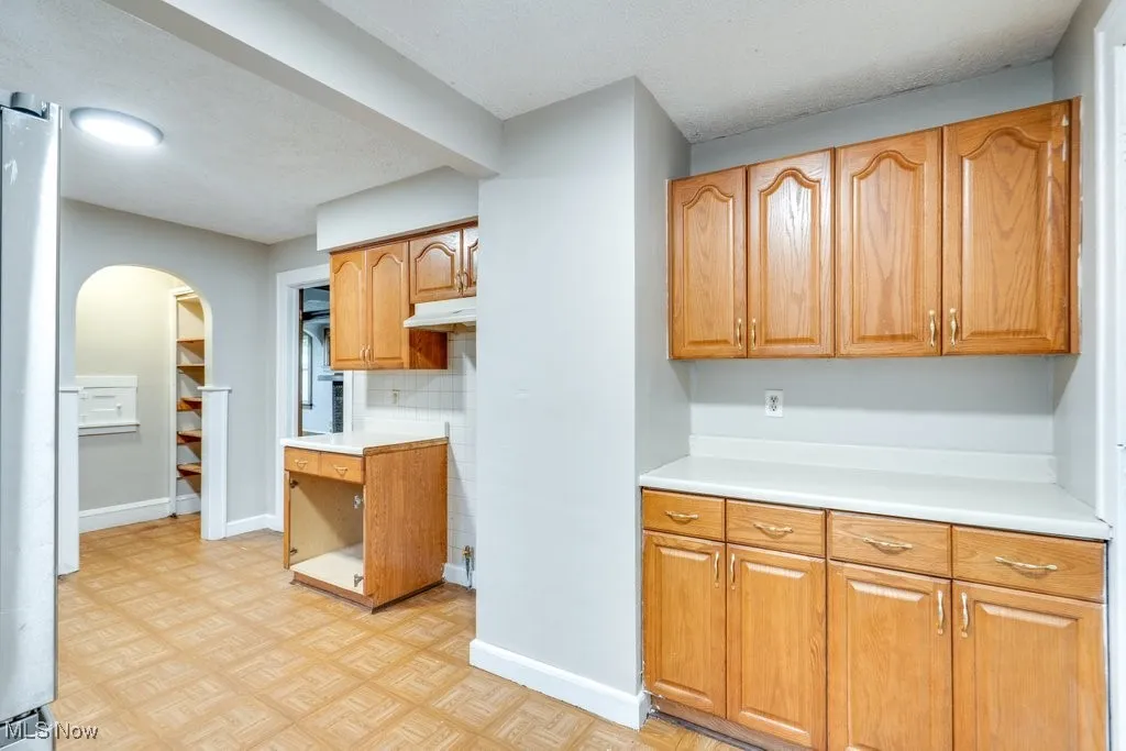 Kitchen with light countertops, arched walkways, under cabinet range hood, baseboards, and a textured ceiling